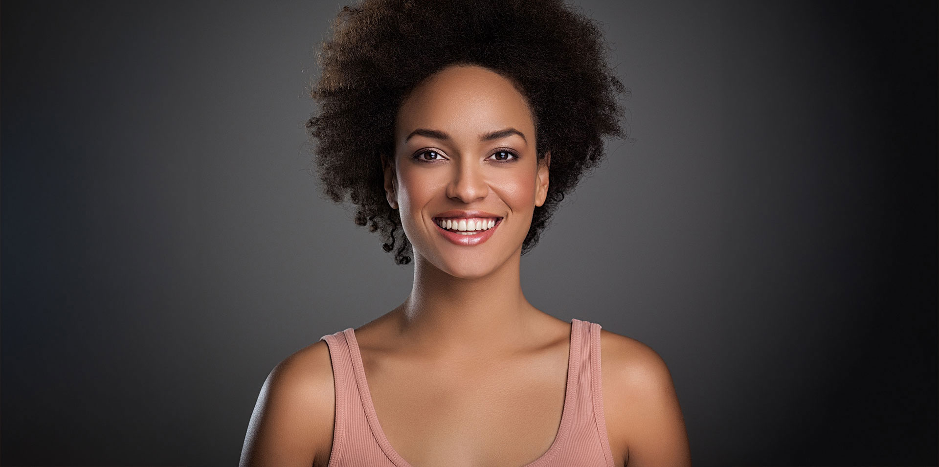 The image features a smiling woman with short hair, wearing a light-colored top, against a dark background.