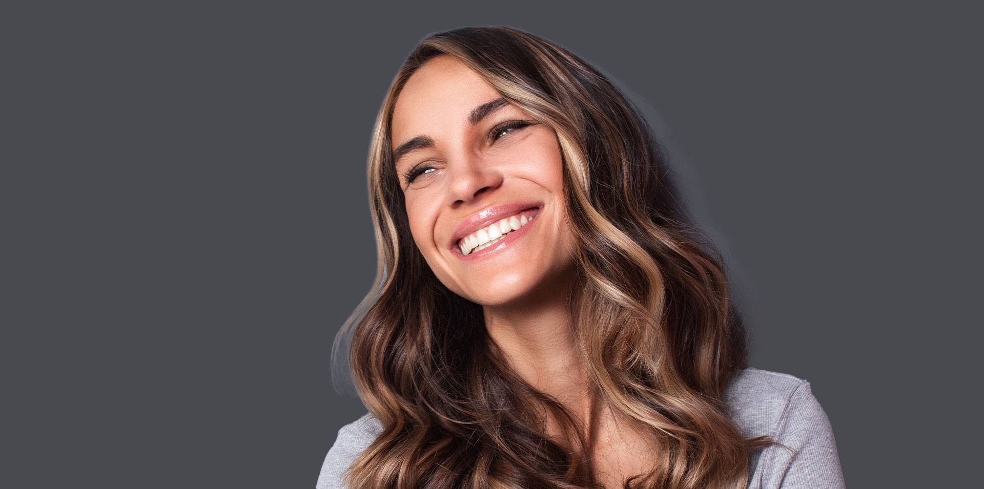A woman with brown hair and a smile, wearing a light-colored top.