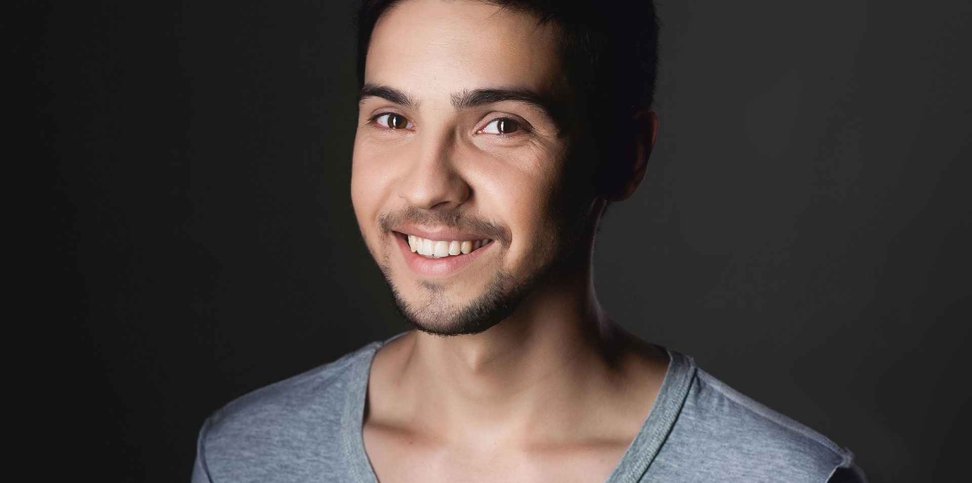 This image shows a man with a beard smiling at the camera against a dark background.